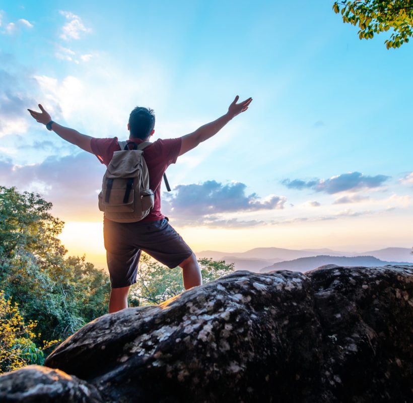 Rear view back of Young asian hiking man standing and rise-up hands with happy on peak of rocky mountain, copy space